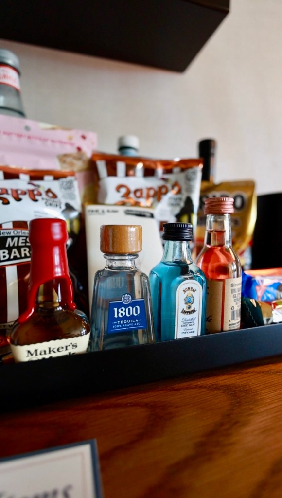 Assorted miniature liquor bottles arranged on a bar tray inside a guest room at The Harper Hotel